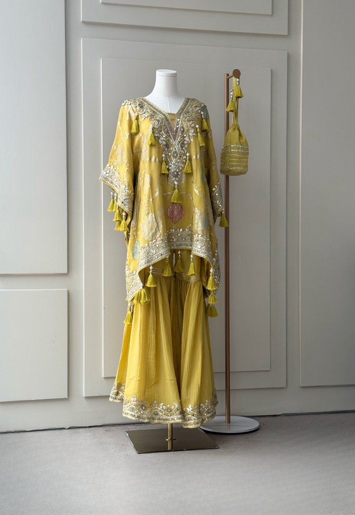 yellow embroidered kurta set with intricate mirror work, sequins, and tassel details, paired with flowy sharara pants and a matching embellished potli bag. Perfect for festive occasions and weddings