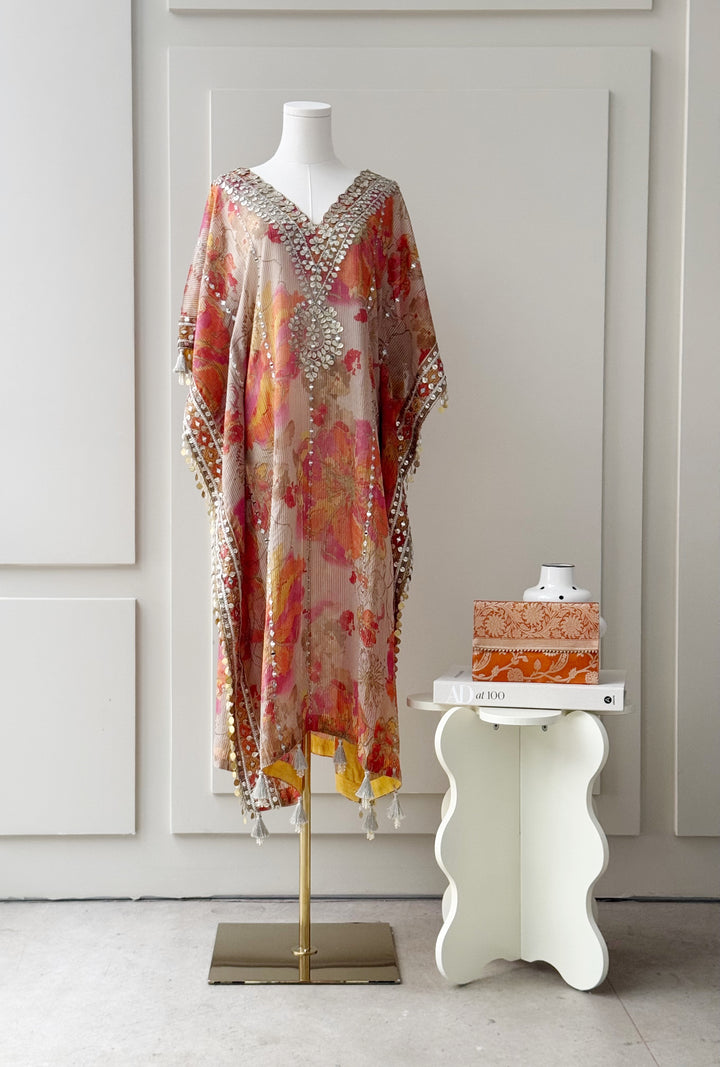 Floral printed kaftan in orange, pink, and yellow hues with intricate mirror work on the neckline and borders, finished with tassel details, ideal for festive and casual occasions