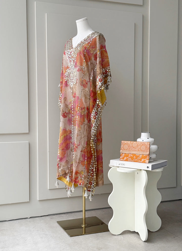 Floral printed kaftan in orange, pink, and yellow hues with intricate mirror work on the neckline and borders, finished with tassel details, ideal for festive and casual occasions