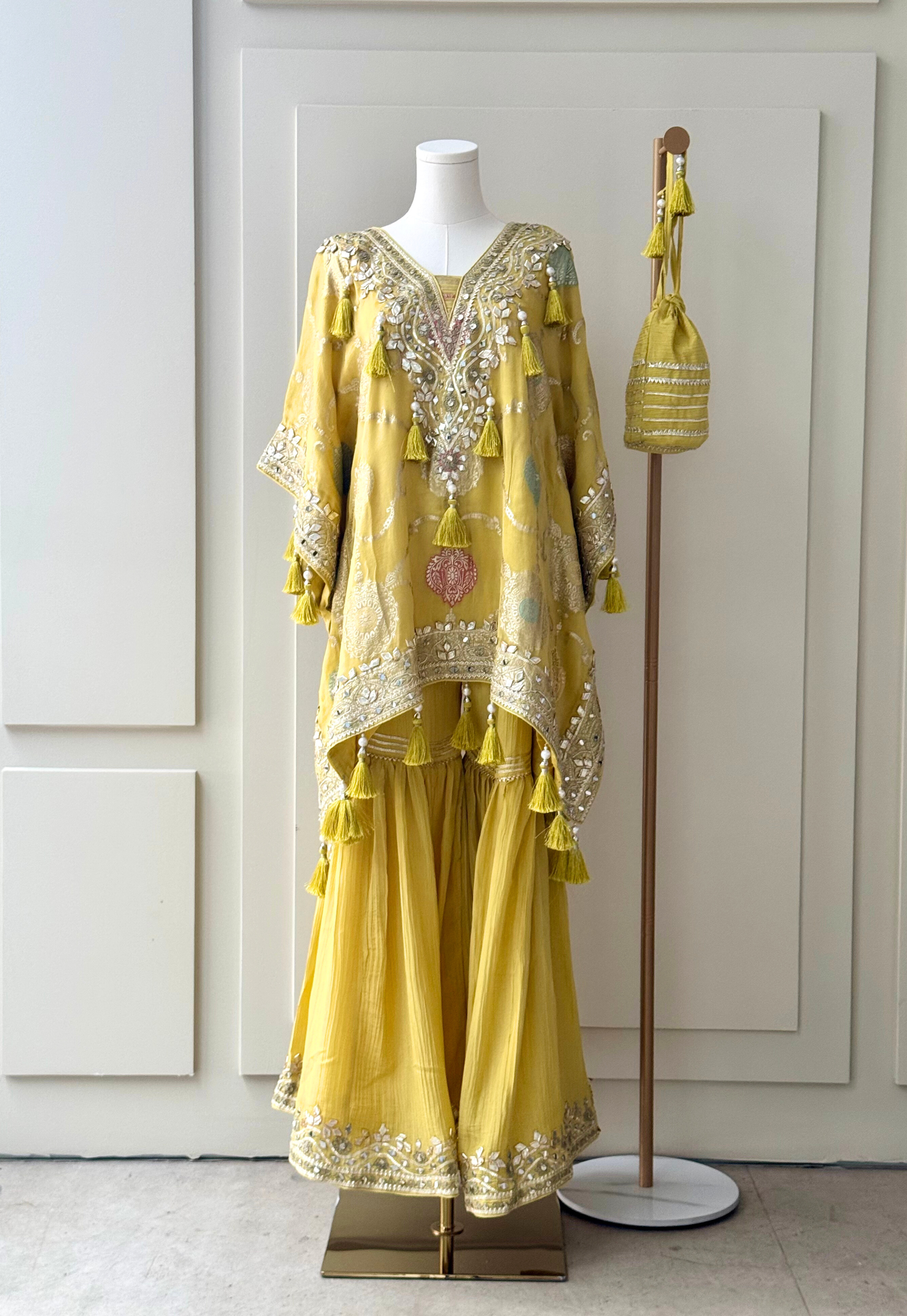 yellow embroidered kurta set with intricate mirror work, sequins, and tassel details, paired with flowy sharara pants and a matching embellished potli bag. Perfect for festive occasions and weddings