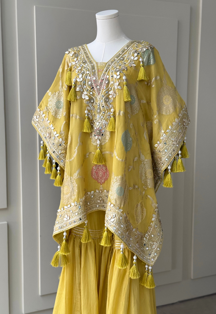 yellow embroidered kurta set with intricate mirror work, sequins, and tassel details, paired with flowy sharara pants and a matching embellished potli bag. Perfect for festive occasions and weddings